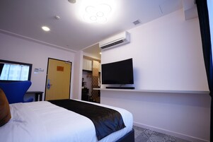 A hotel room with a bed, a television mounted on the wall, an air conditioning unit, and a door leading to a bathroom.