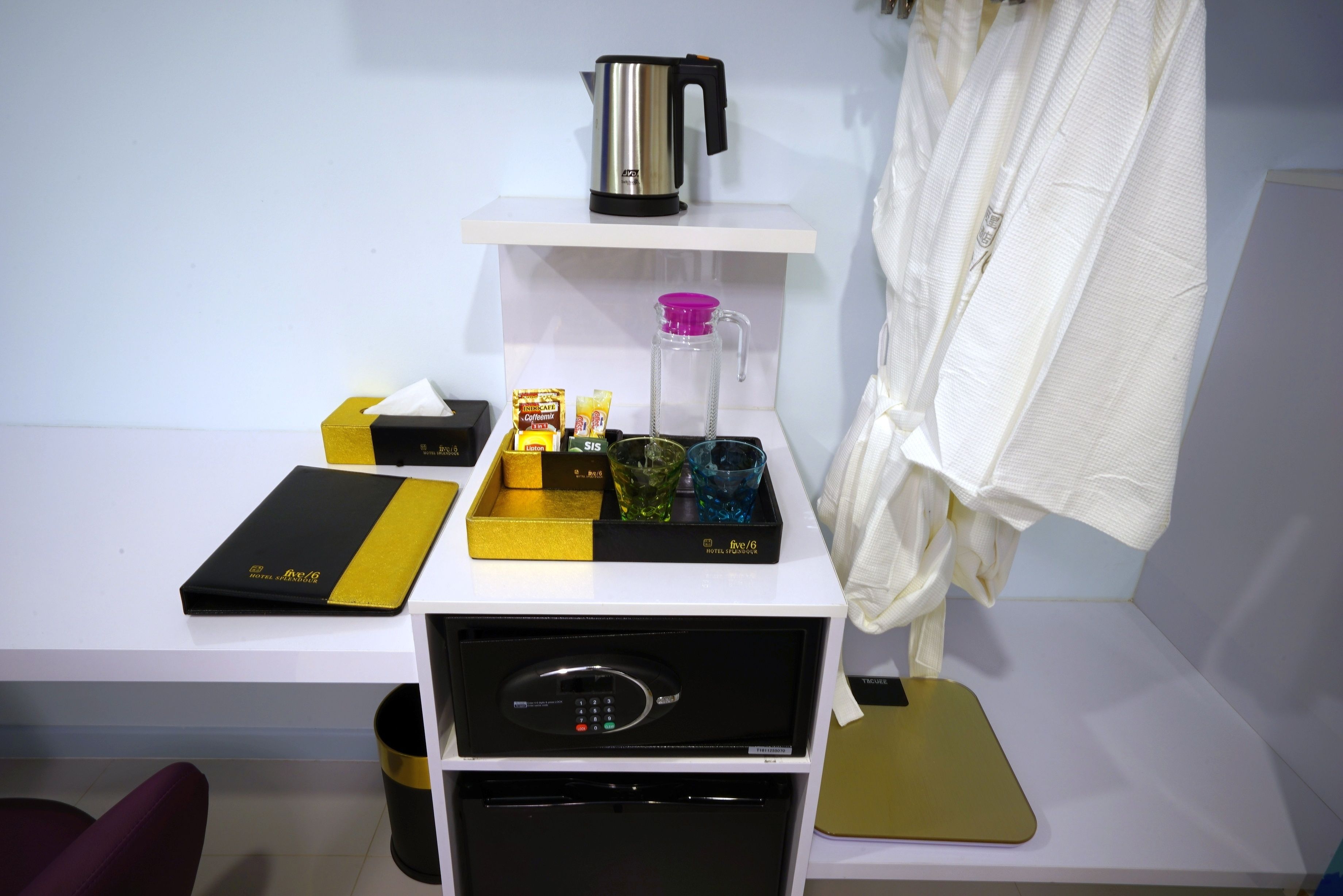 Een hotelkamer met een wit bureau, een zwart en gouden dienblad met toiletartikelen, een koffiezetapparaat en een minibar.