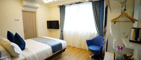 Habitació d'hotel amb un llit, una cadira, una televisió i una finestra amb cortines.