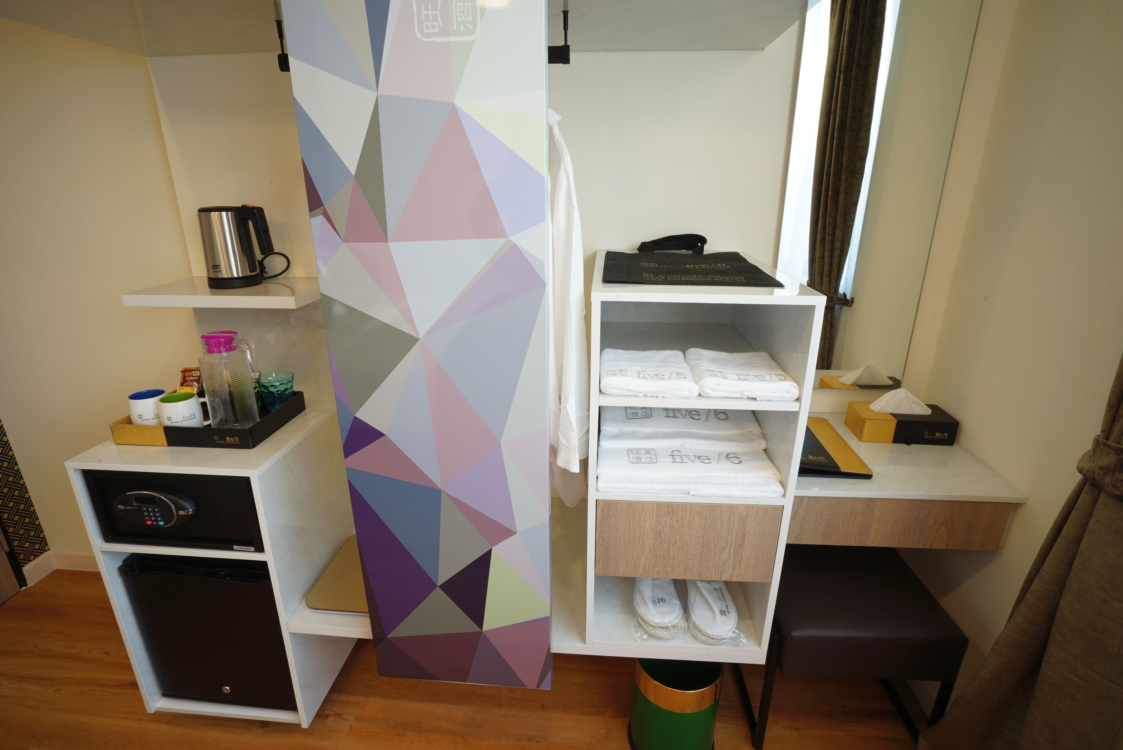 Une chambre d’hôtel compacte comprenant un coin cuisine, un lit, un petit bureau et un espace de rangement contenant des serviettes et des articles de toilette.