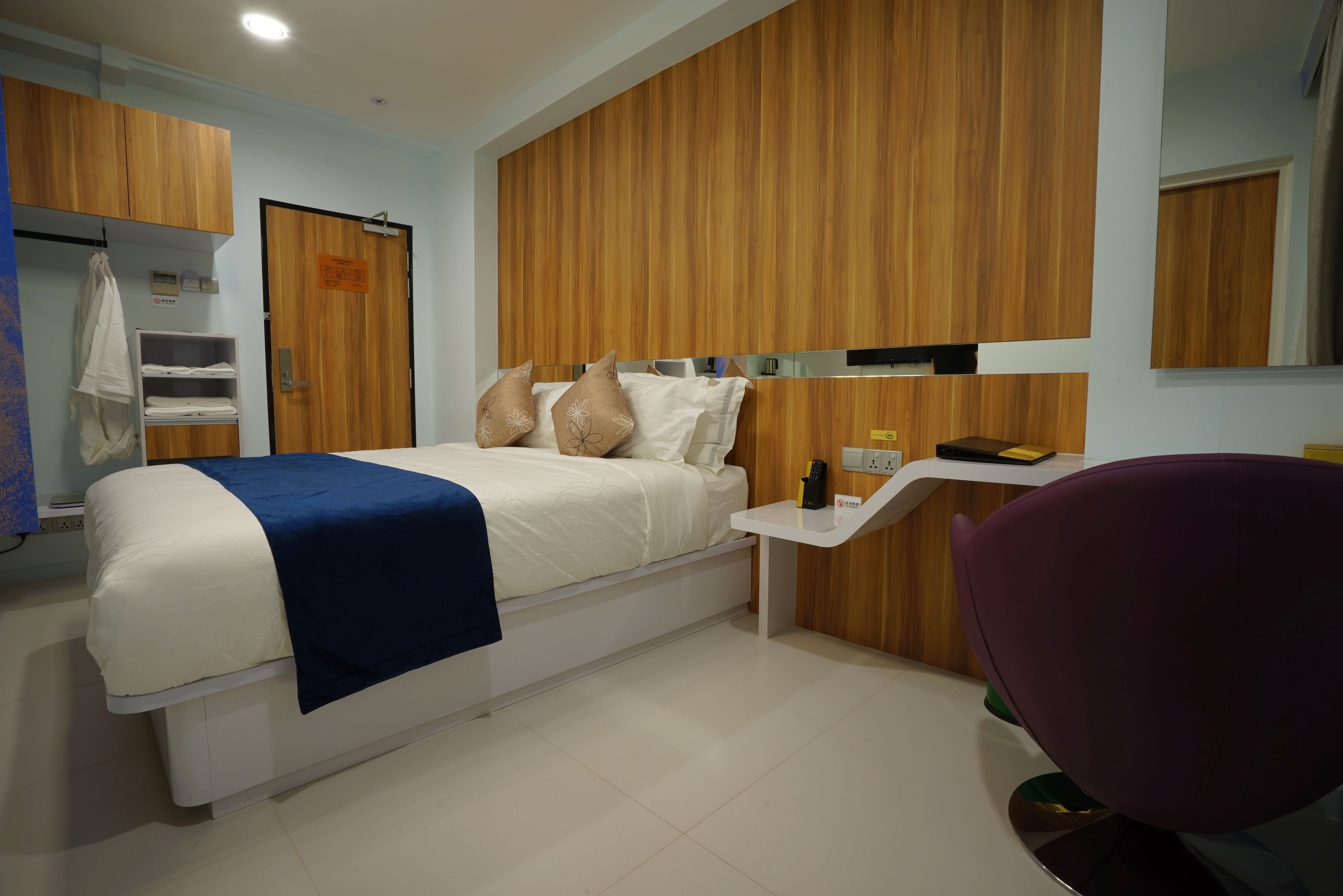 A modern hotel room with a bed, bedside table, chair, and wooden panel walls.