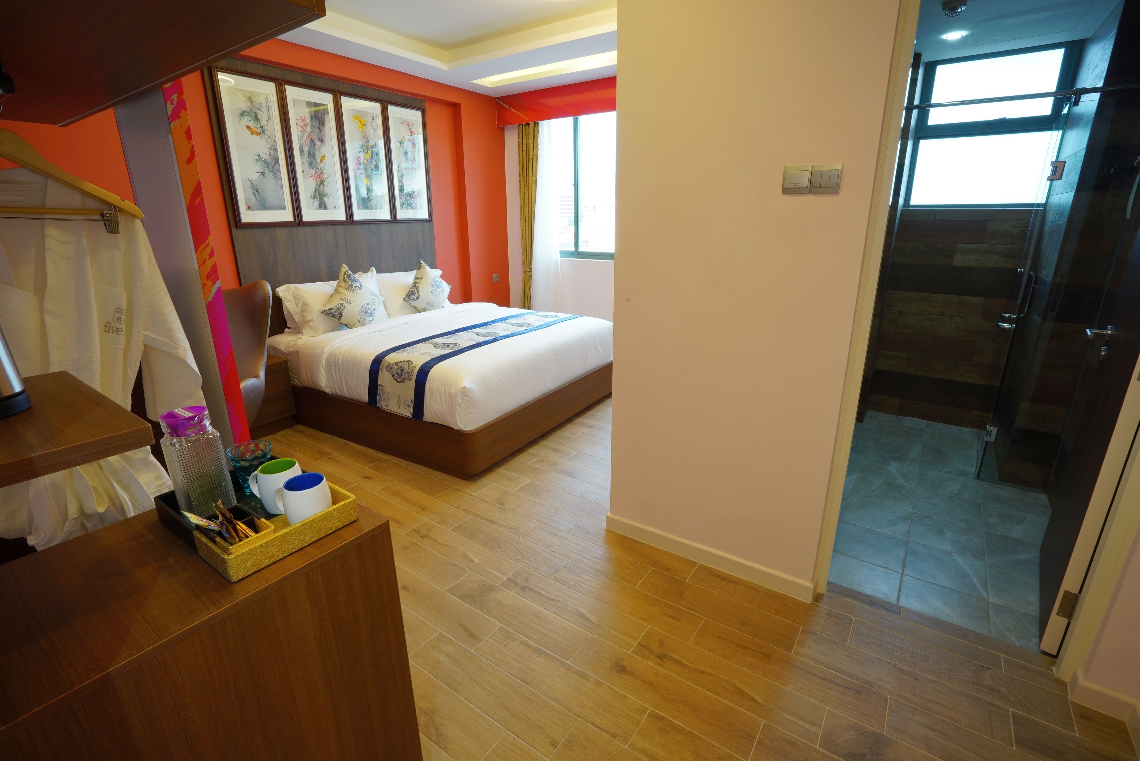 A hotel room with a bed, wooden floor, a desk with a tray of toiletries, and a window with curtains.