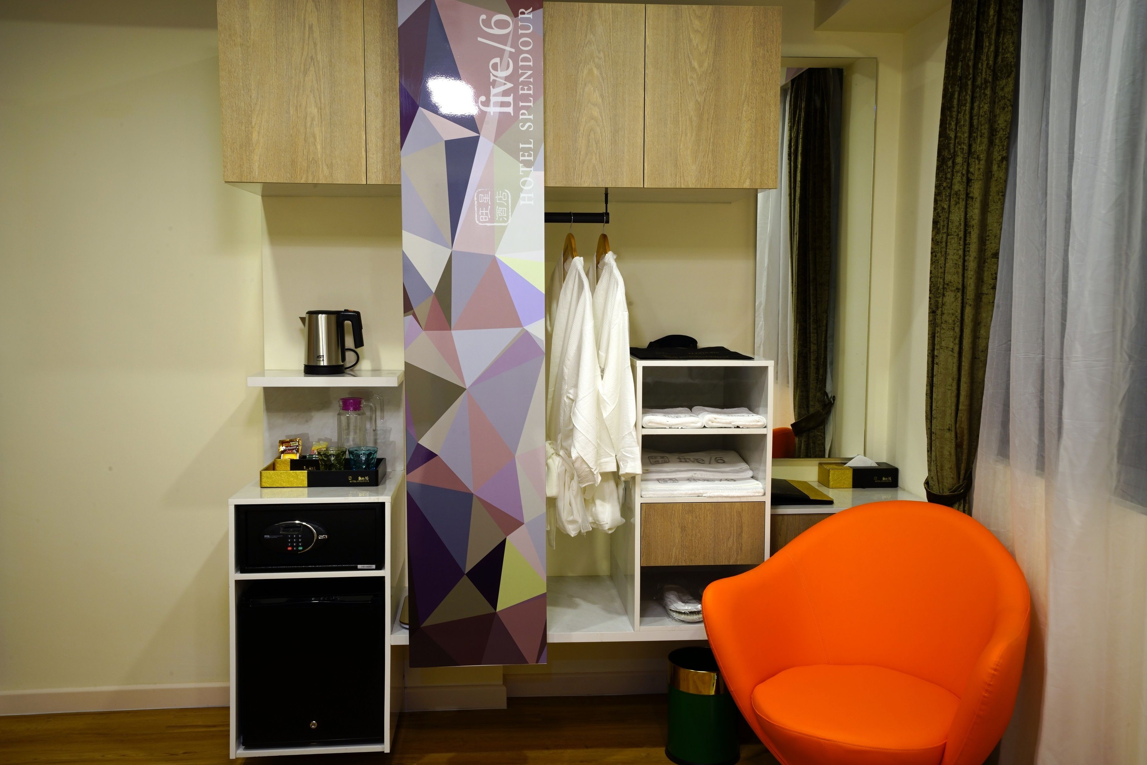 A hotel room with a kitchenette, a wardrobe, a seating area, and a large window with curtains.