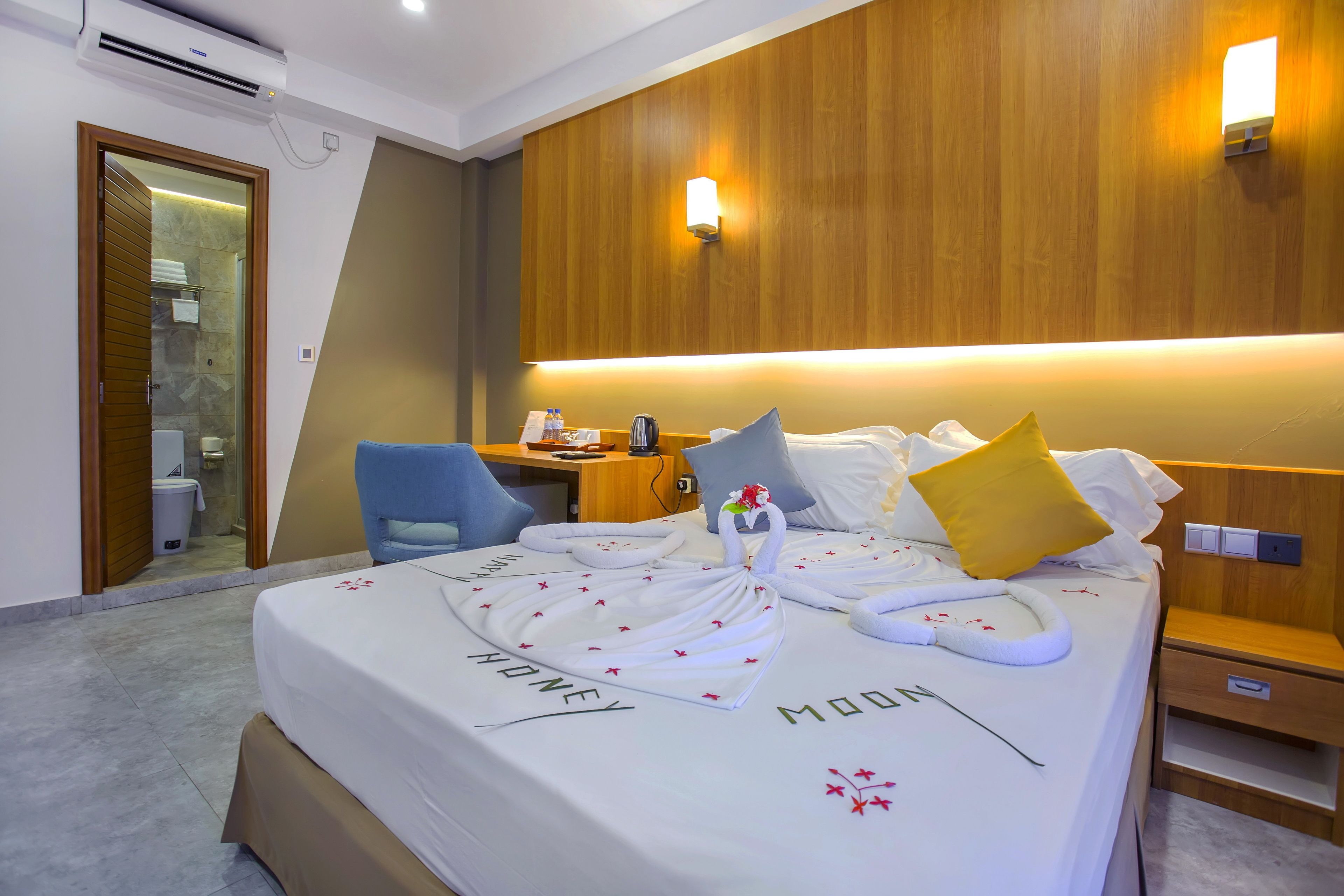 Een hotelkamer met een opgemaakt bed, een bureau met stoel, een nachtkastje en een houten hoofdbord.