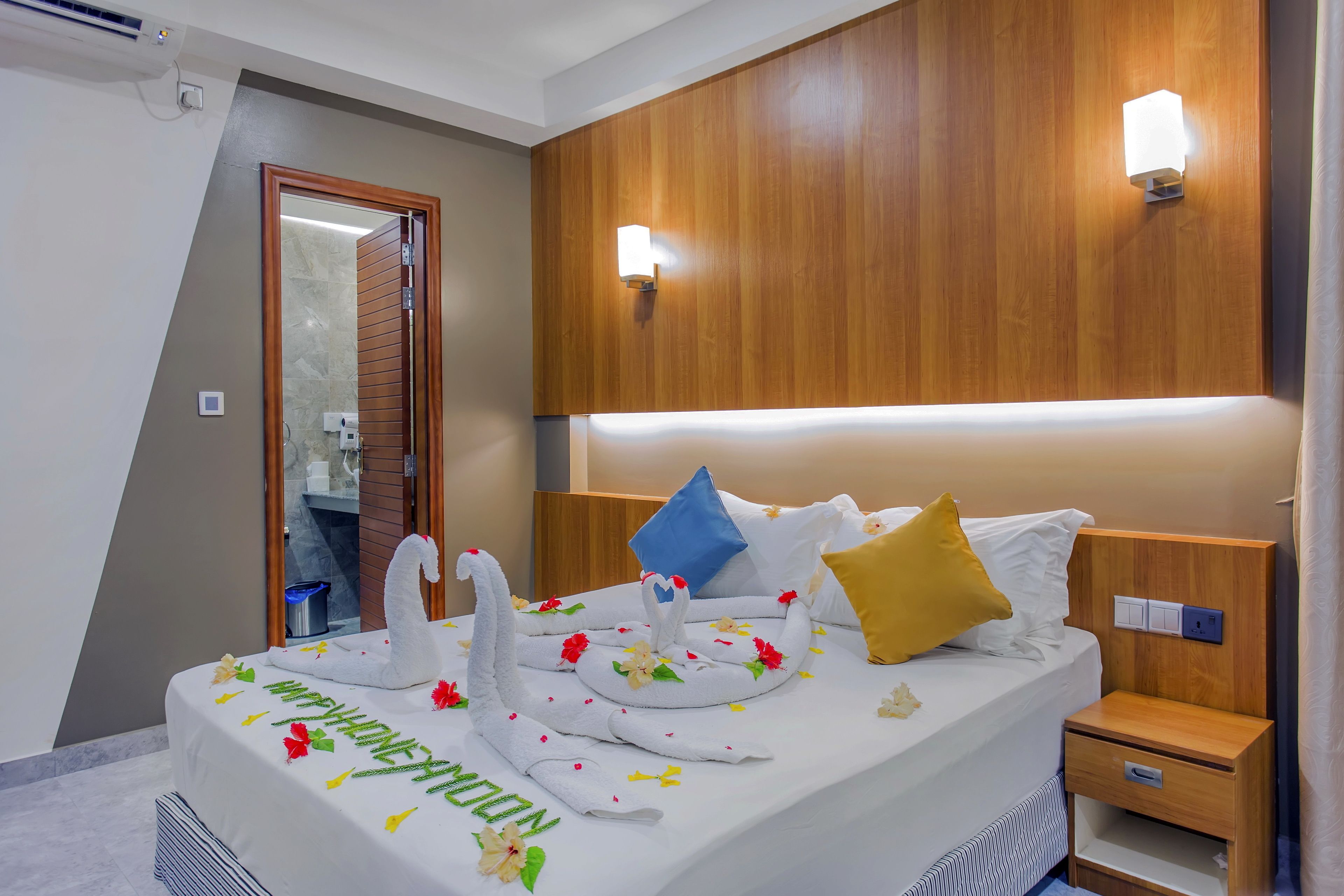 A hotel room with a neatly made bed, a wooden headboard, bedside lamps, and a small bedside table.
