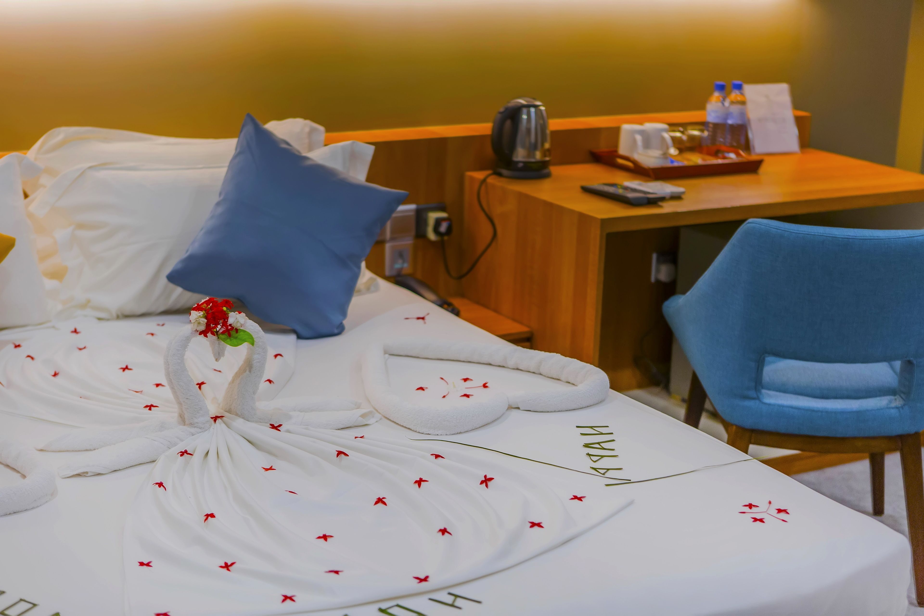 Una cama bien hecha con un diseño de toalla con forma de cisne, una almohada azul y un pequeño ramo de flores.