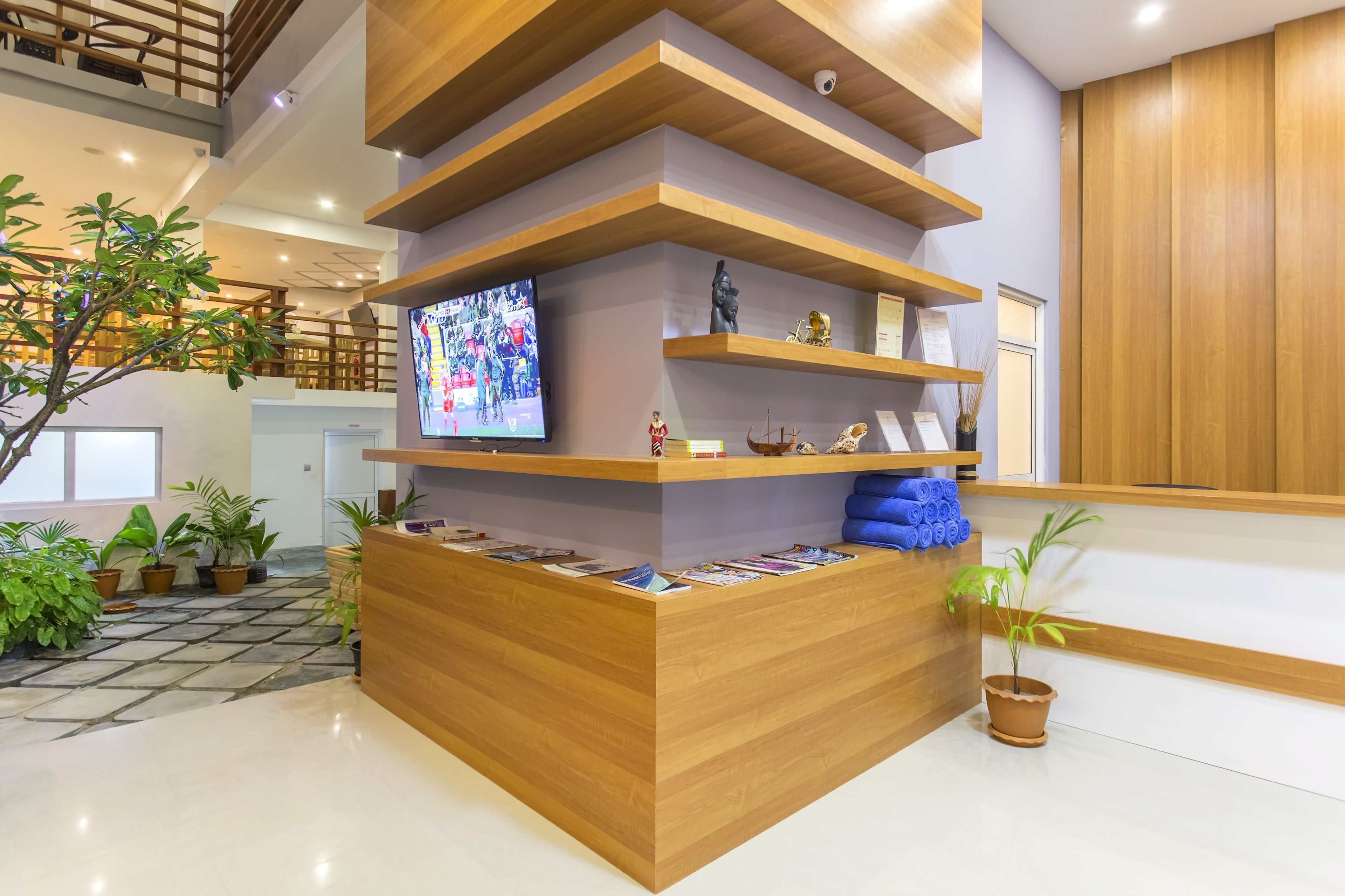 A reception desk with a television, potted plants, and wooden shelves.