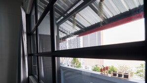 A balcony with a view of the city, a window with a metal frame, and a white air conditioner. - Pann Residence (Bangkok)