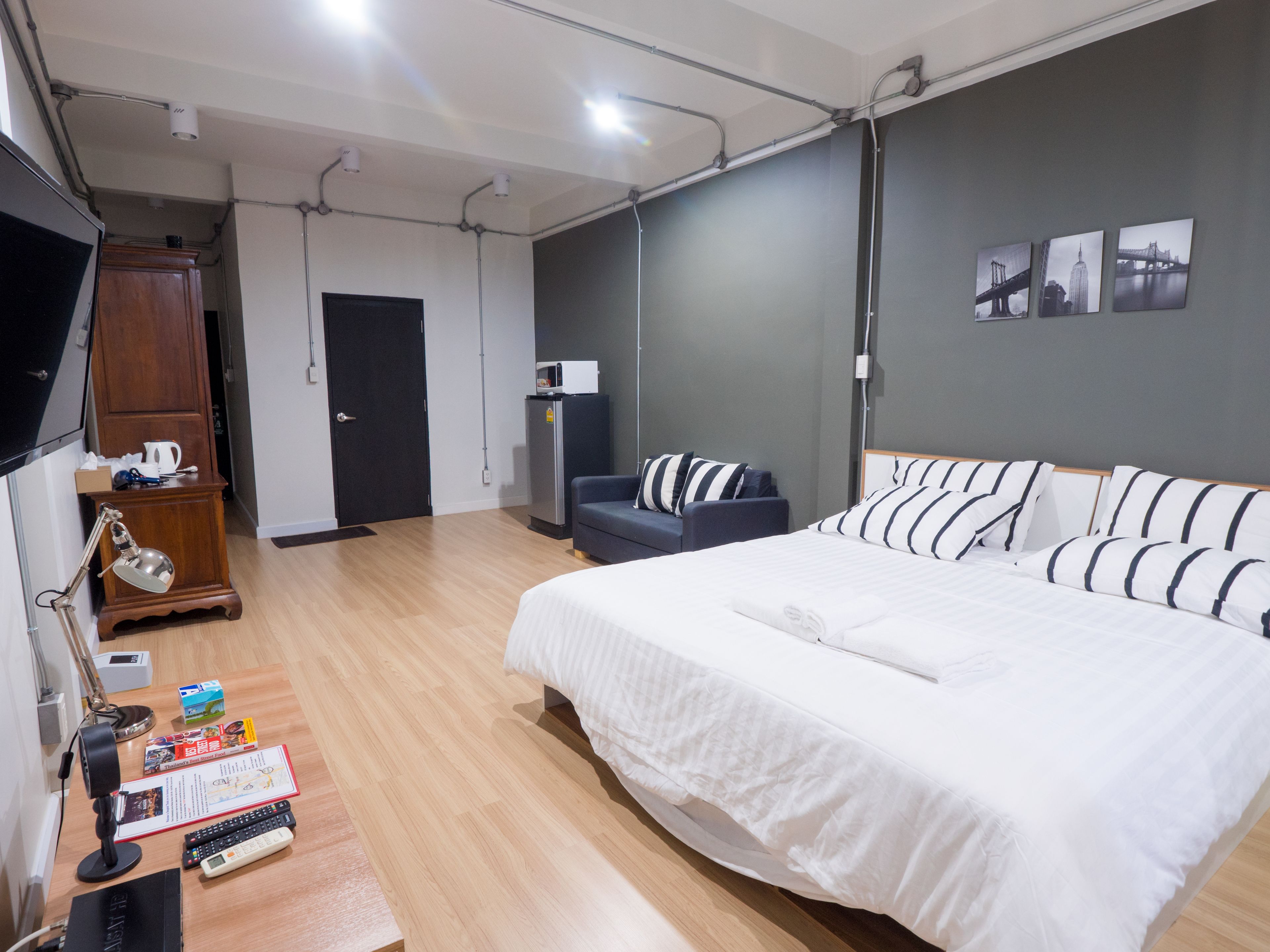 A hotel room with a large bed, a desk with a lamp, a wardrobe, and a refrigerator.