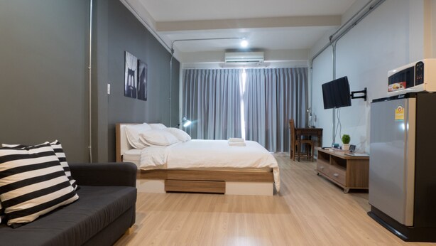 A modern hotel room with a bed, a sofa, a TV, a refrigerator, and a desk. - Pann Residence (Bangkok)