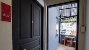 A modern apartment with a dark wooden door, a small balcony with wooden furniture, and a city view. - Pann Residence (Bangkok)