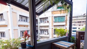 A balcony with a table and chairs, potted plants, and a view of surrounding buildings. - Pann Residence (Bangkok)
