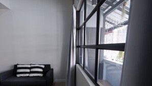 A modern room with a dark sofa, a large window with curtains, and a view of the outside. - Pann Residence (Bangkok)