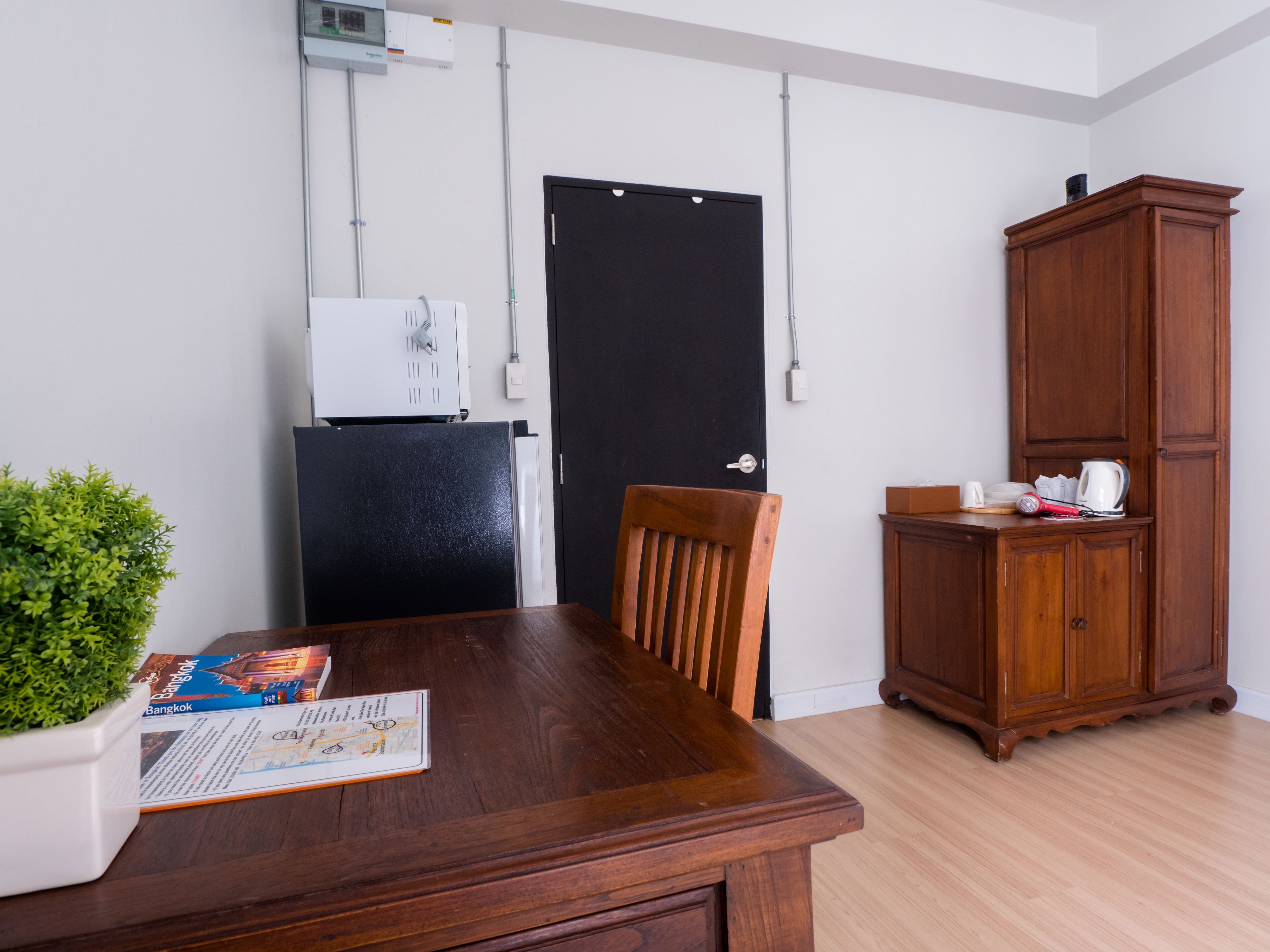 A dining area with a wooden table, a chair, a cabinet, a potted plant, and a refrigerator.