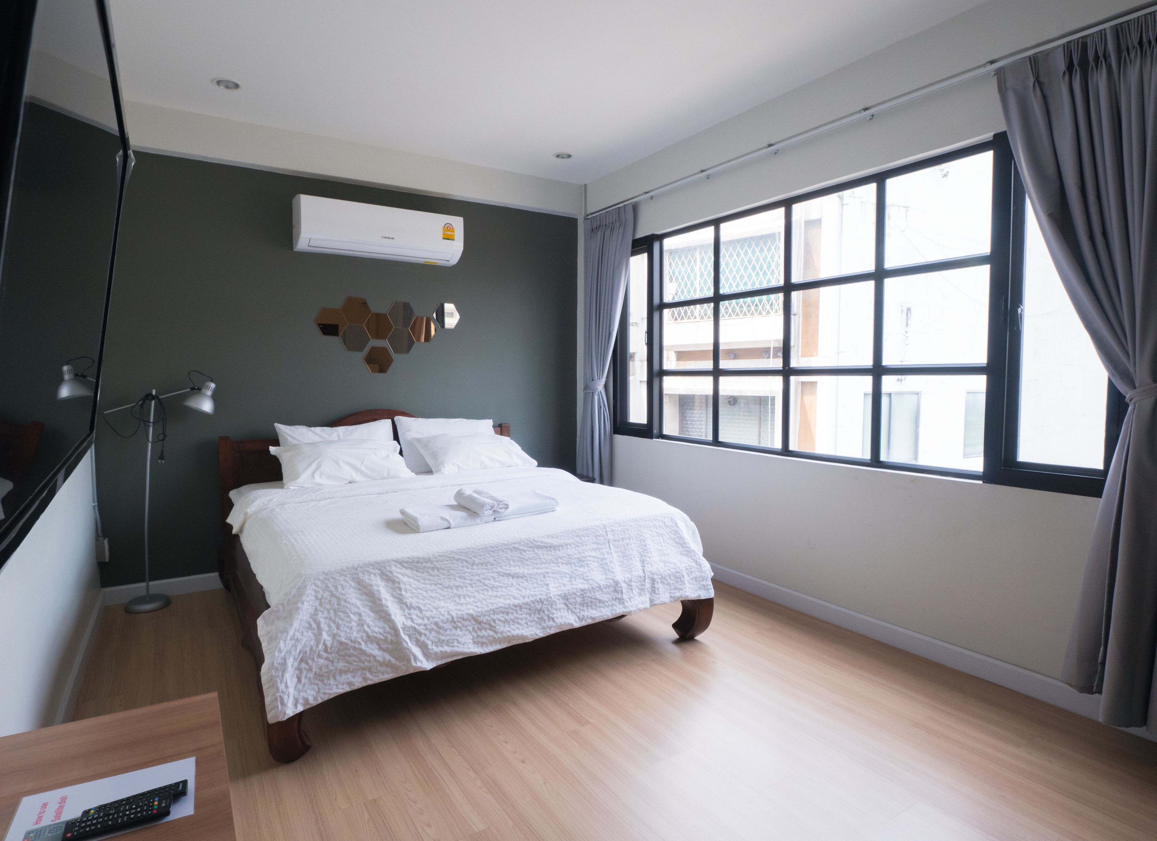 A neatly made bed with white linens, a bedside lamp, and a wall-mounted air conditioner.