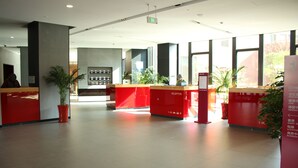 Un'ampia hall con reception rosse, piante in vaso e una visuale libera sull'uscita.