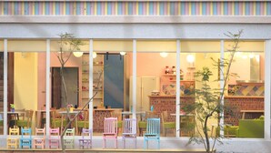 A brightly lit cafe with colorful chairs and tables, large windows, and a brick wall interior.