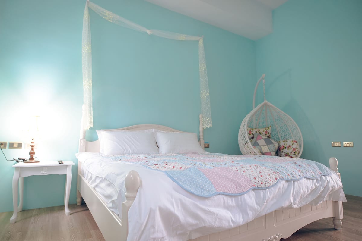 A bedroom with a white bed, a nightstand, a hanging chair, and a light blue wall.