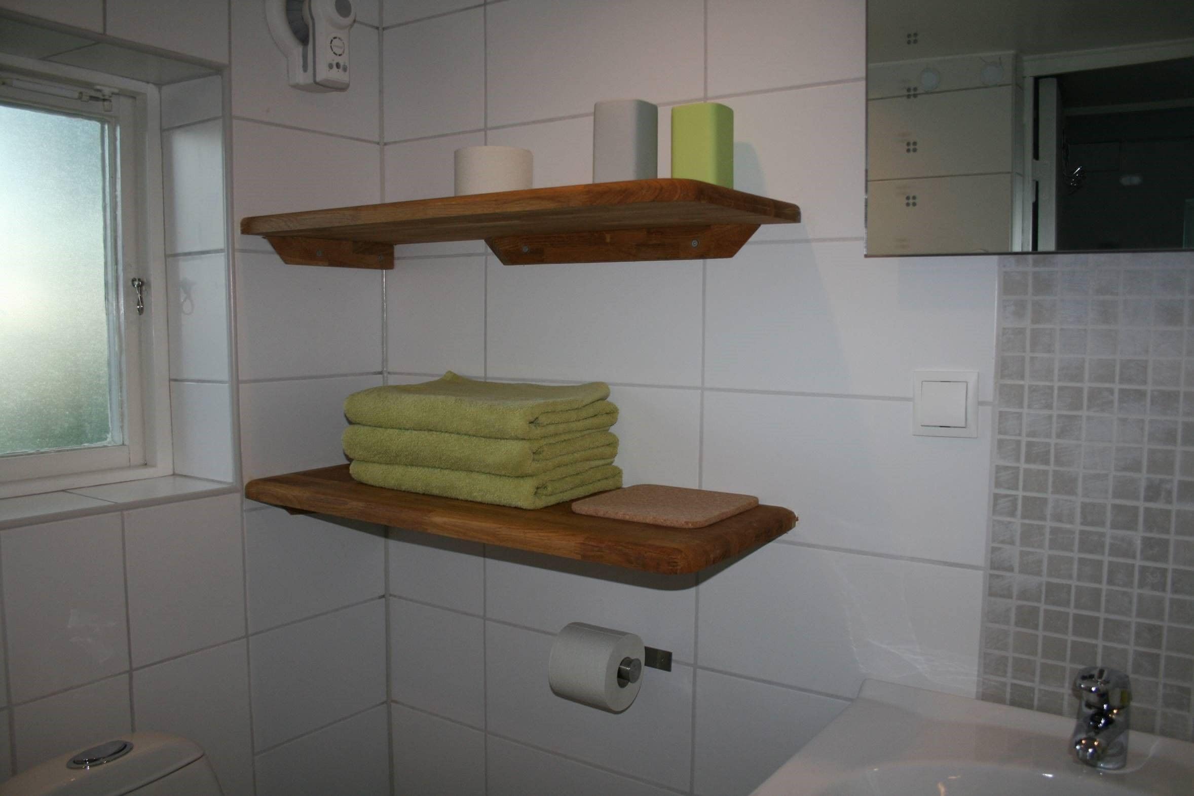 A bathroom with a wooden shelf holding towels and a toilet paper roll.