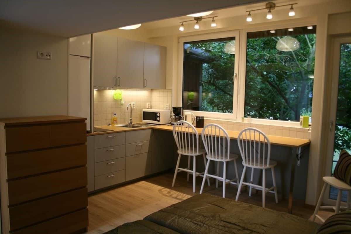 A compact kitchen with a window, white cabinets, and a wooden chest of drawers.