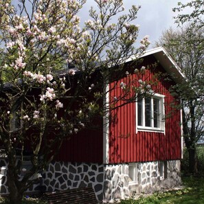 A red and white house with a stone facade, a window, and a tree with pink blossoms in the foreground. - Lilla Huset på slätten B&B (Lund)