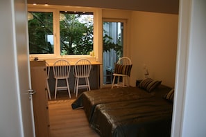 A bedroom with a bed, two chairs, a desk, and a window with a view of trees. - Lilla Huset på slätten B&B (Lund)