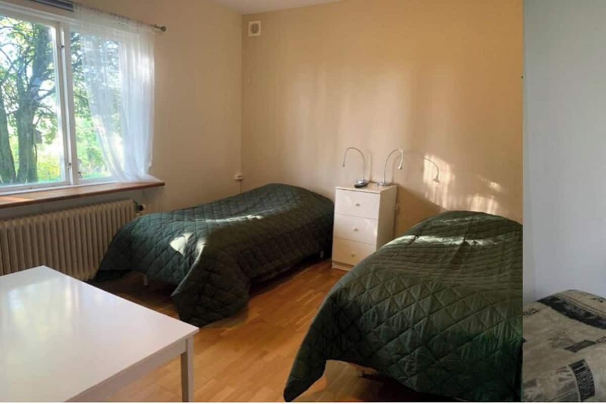 A compact room with two beds, a small kitchenette, a sofa, and a TV.