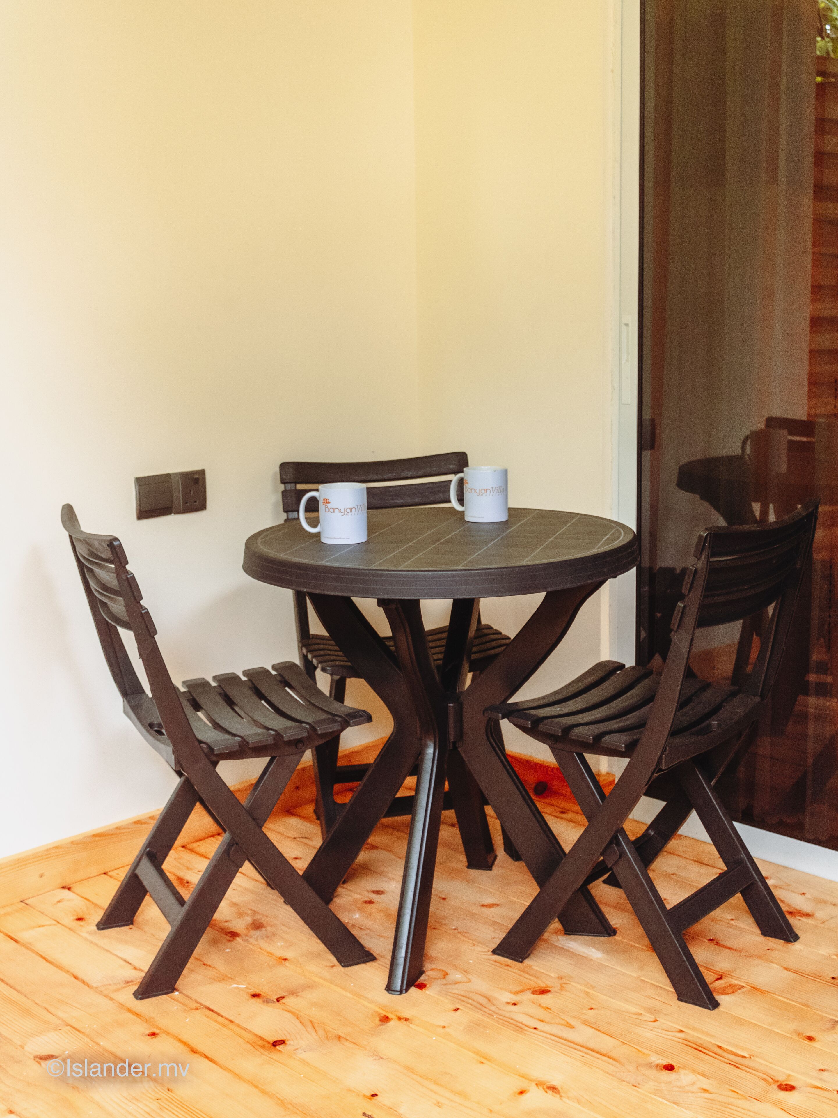 A round table with four chairs, two white mugs on it, and a wooden floor.