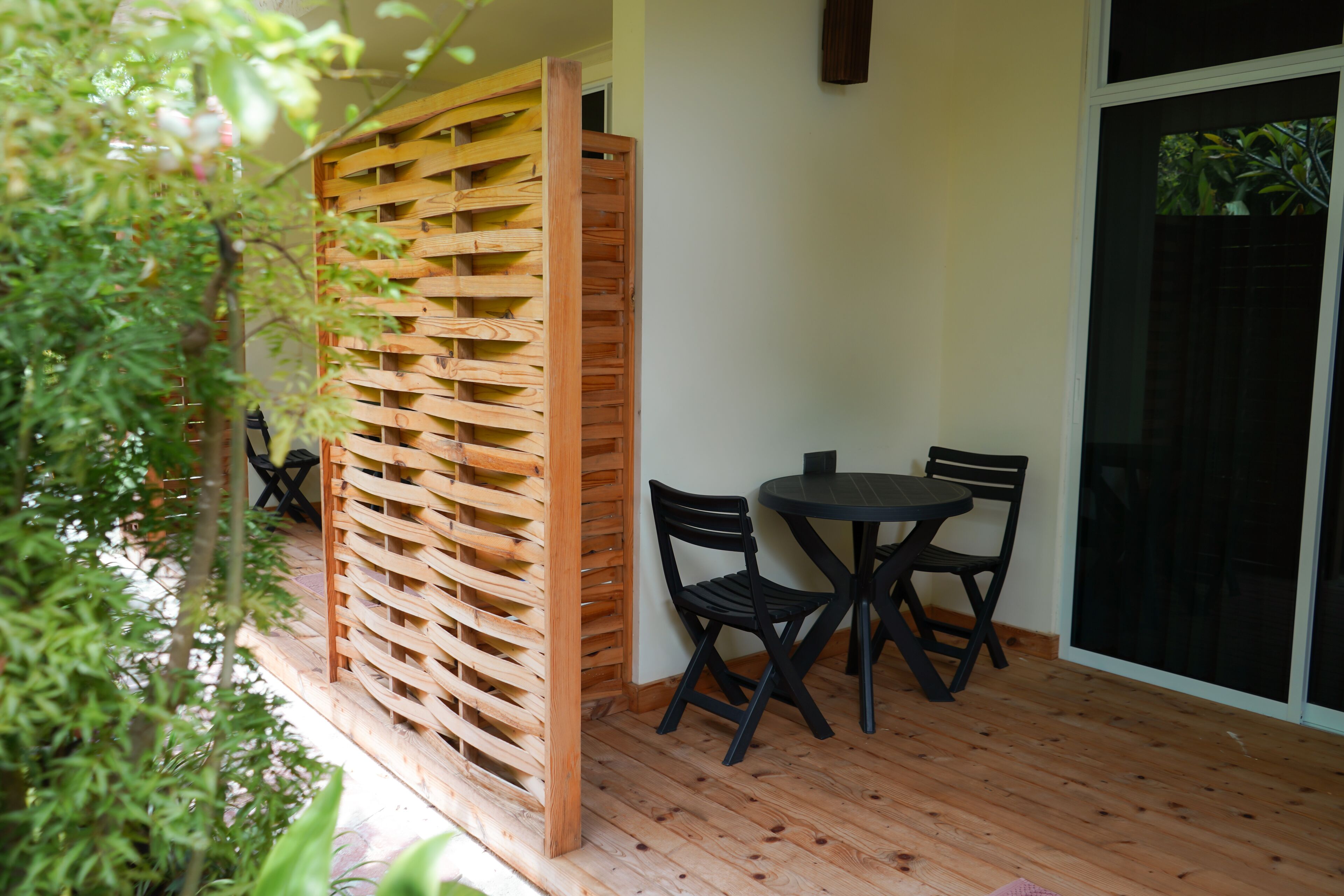 Un espacio de estar al aire libre con madera, que incluye una mesa, sillas y una mampara de madera, además de un ventanal corredero que da a un jardín.