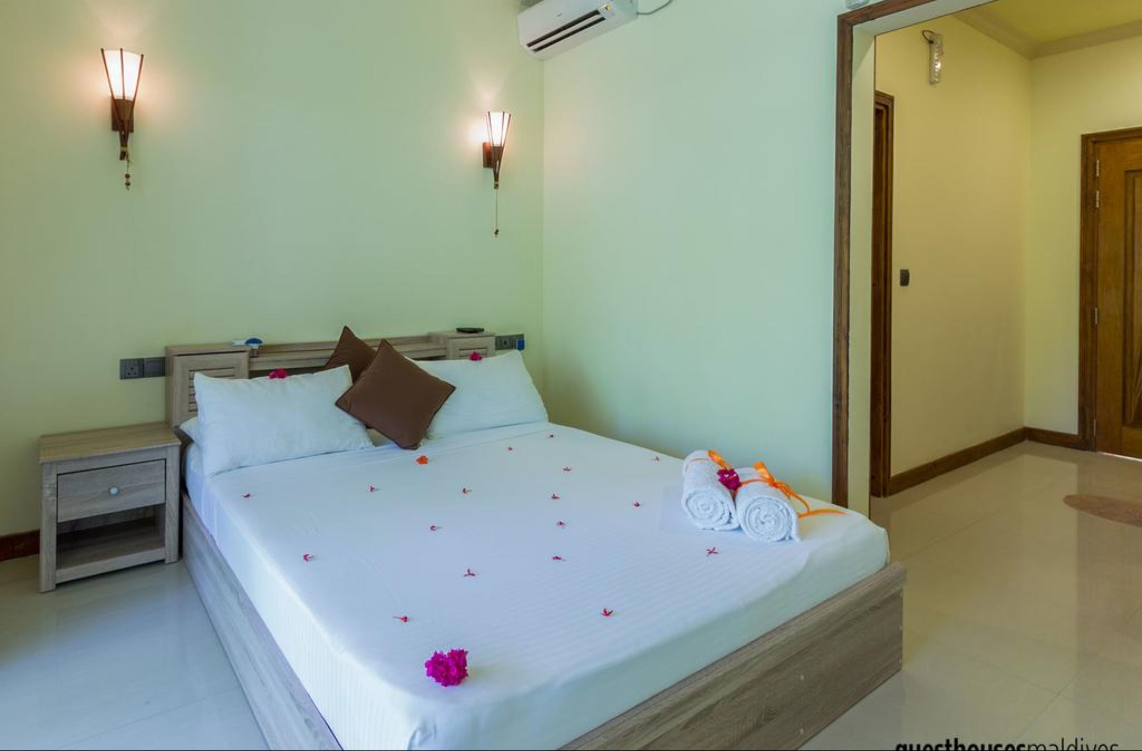 A hotel room with a bed, nightstands, wall sconces, and an air conditioning unit.