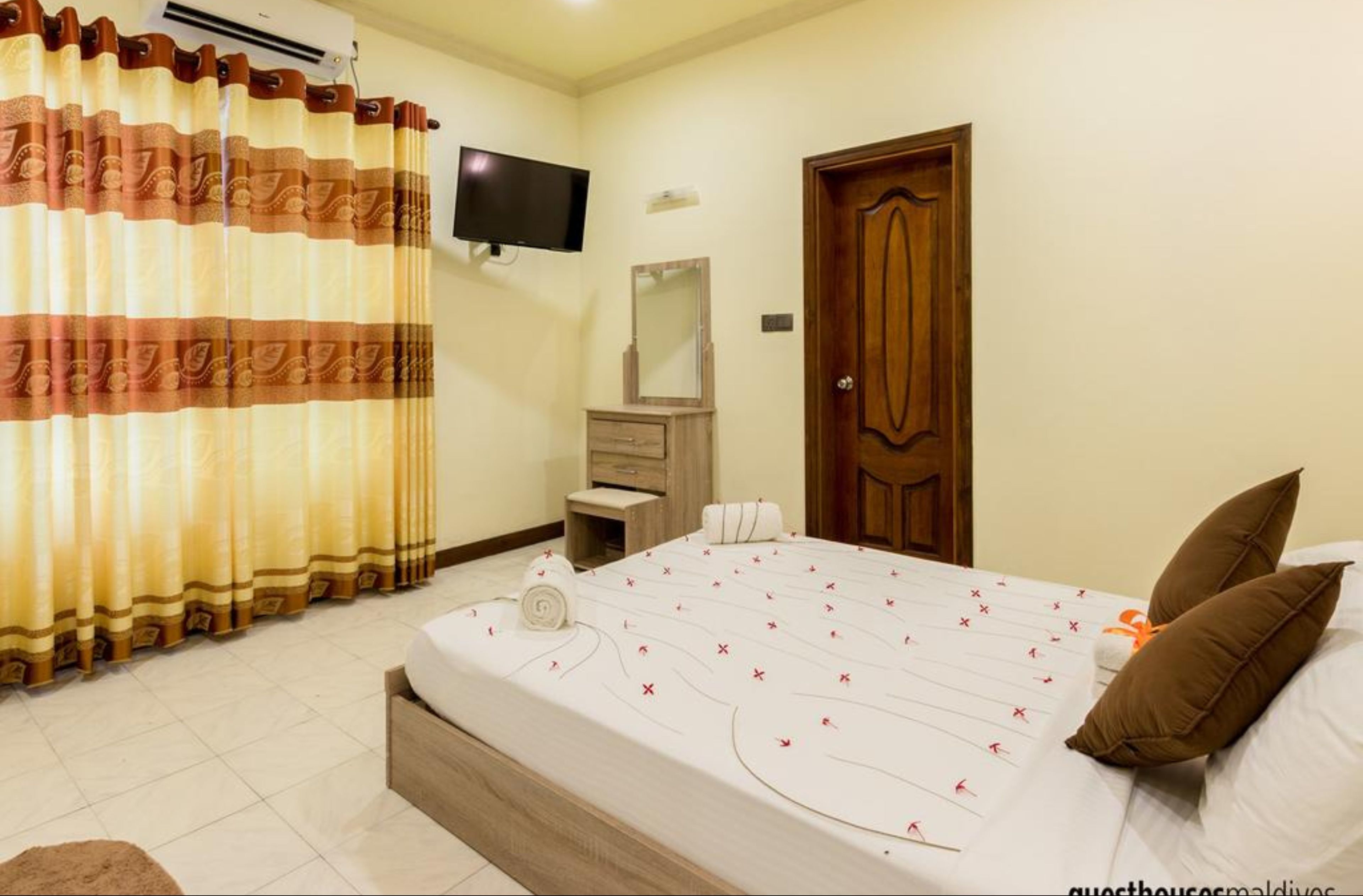 A hotel room with a bed, a TV, a wooden door, and a mirror.