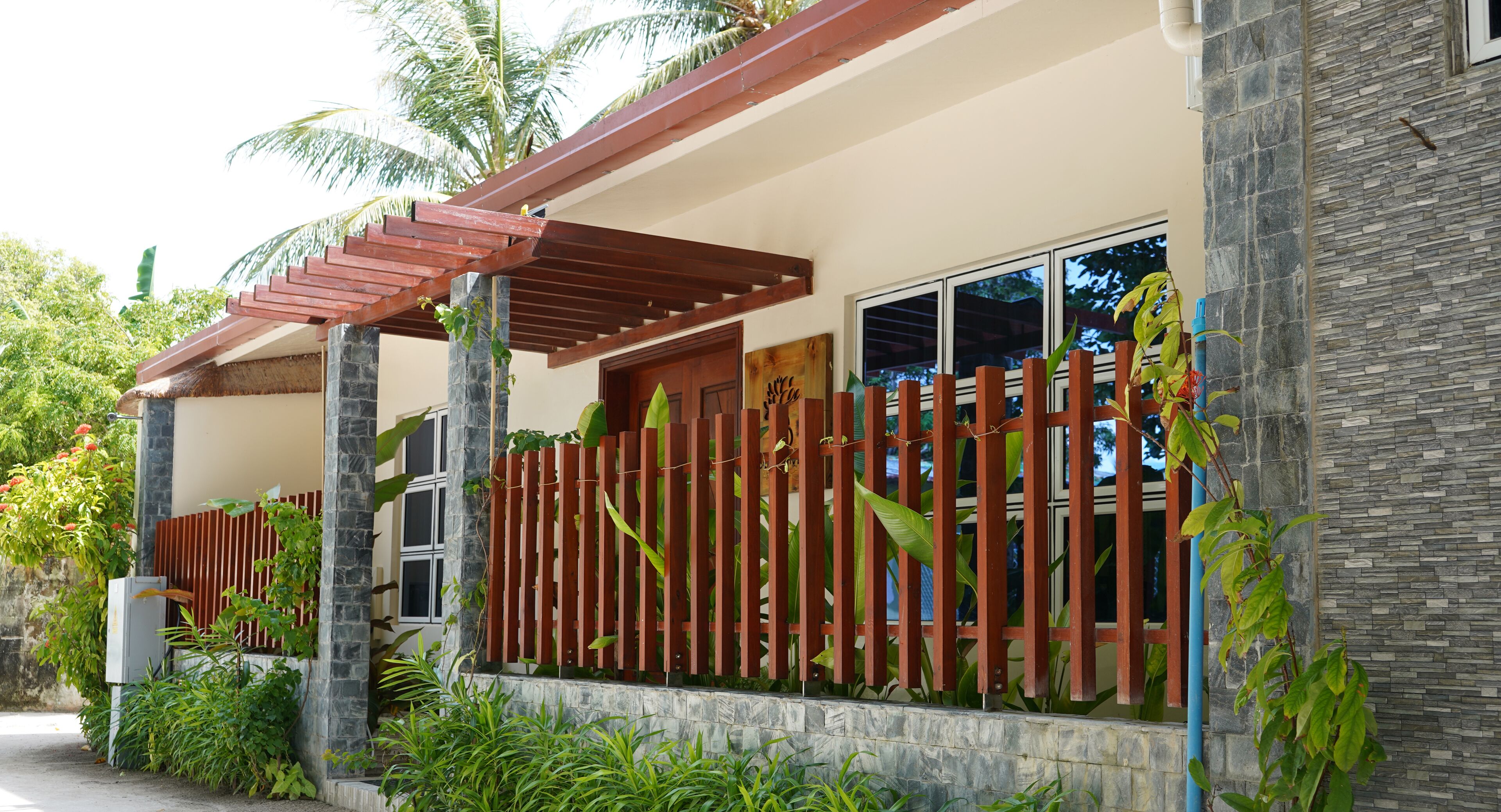 A modern building with a stone facade, a wooden fence, and lush greenery.