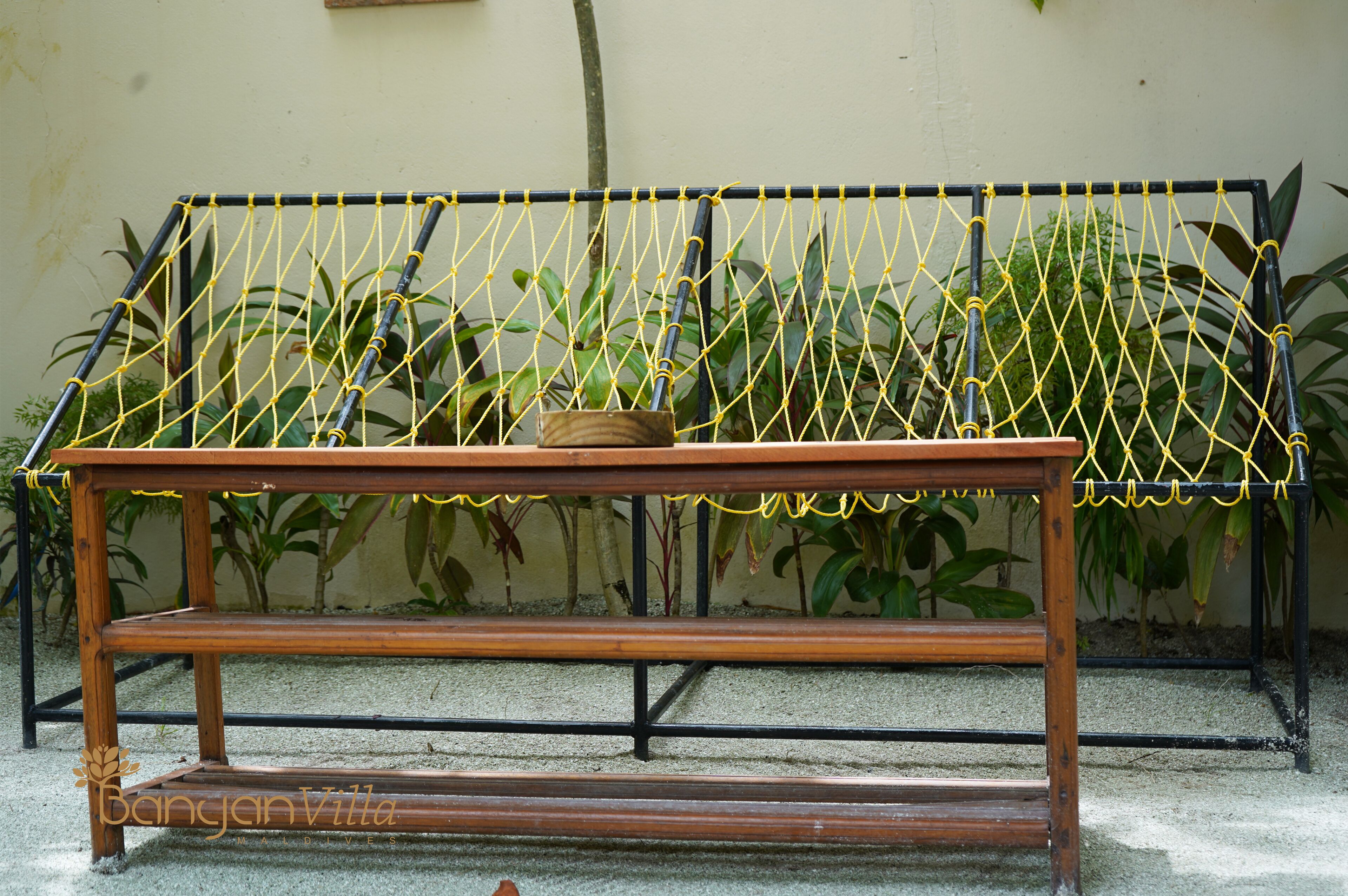 A wooden bench with a netted top, placed against a wall with potted plants.