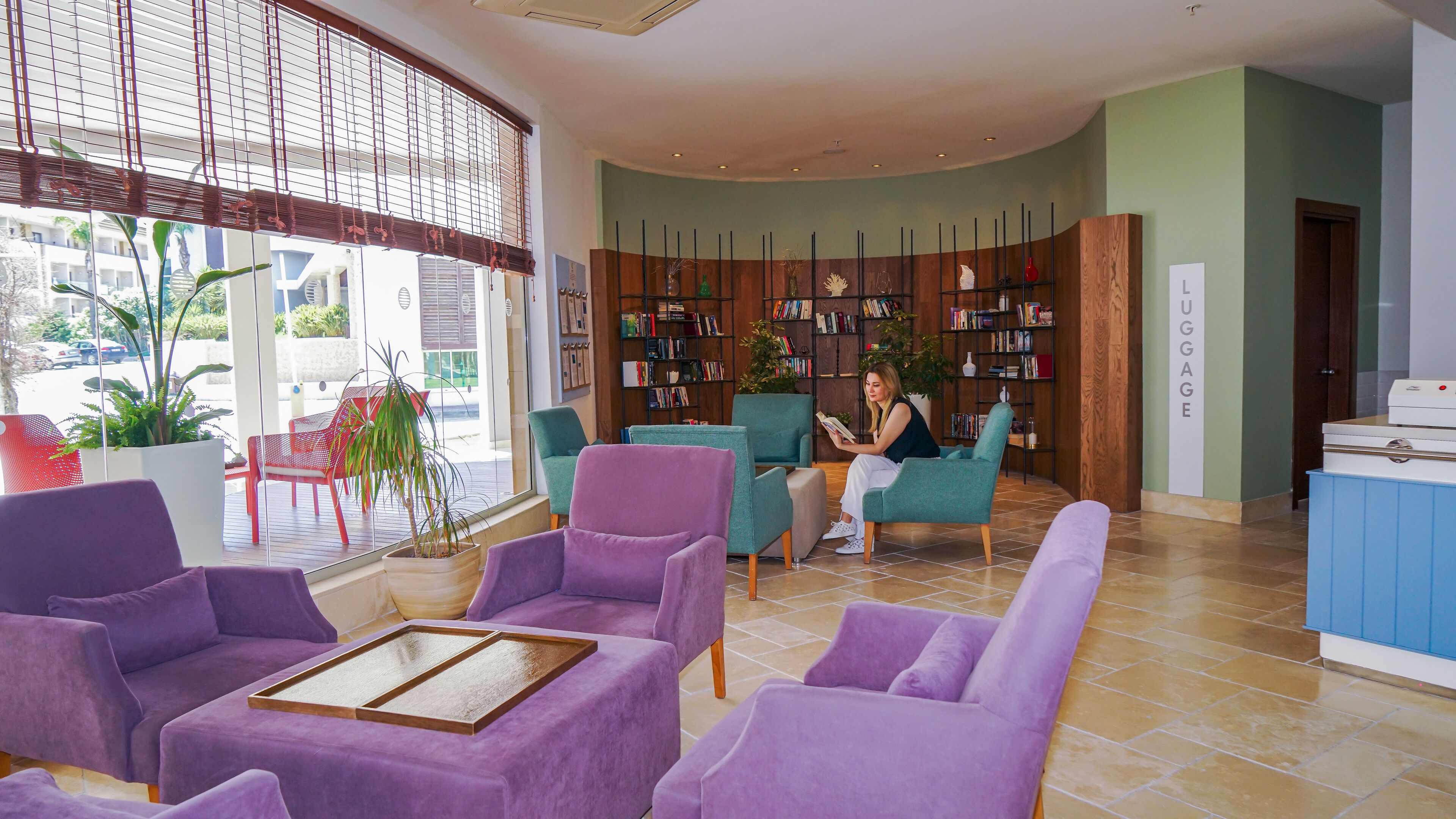 A modern lounge area with purple seating, a large bookshelf, and a view of the outdoors.