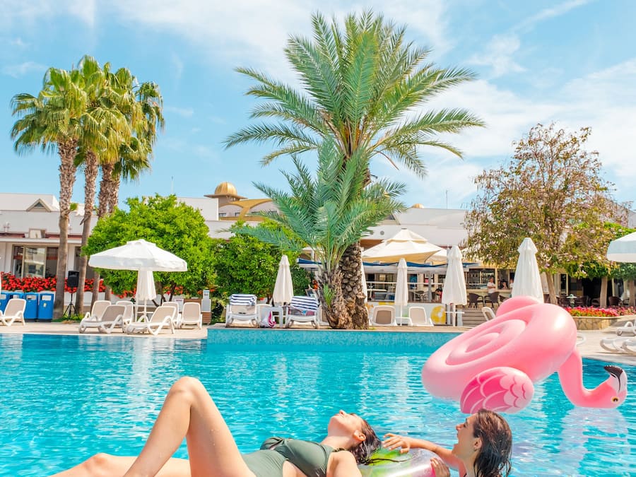 A pool area with lounge chairs, a flamingo float, and a cocktail with a slice of fruit.