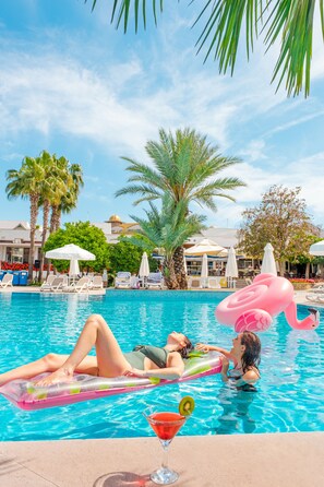 Un área de piscina con sillones de descanso, un flotador de flamenco y un cóctel con una rodaja de fruta.