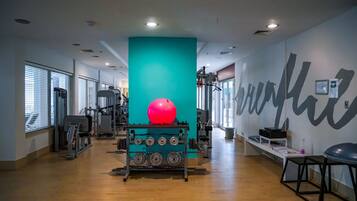 A gym with exercise equipment, a large teal pillar, and a red exercise ball.