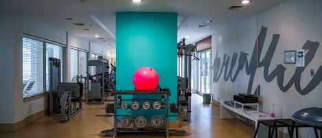 Un gimnasio con equipo de ejercicio, un pilar grande color turquesa y una pelota de ejercicio roja.