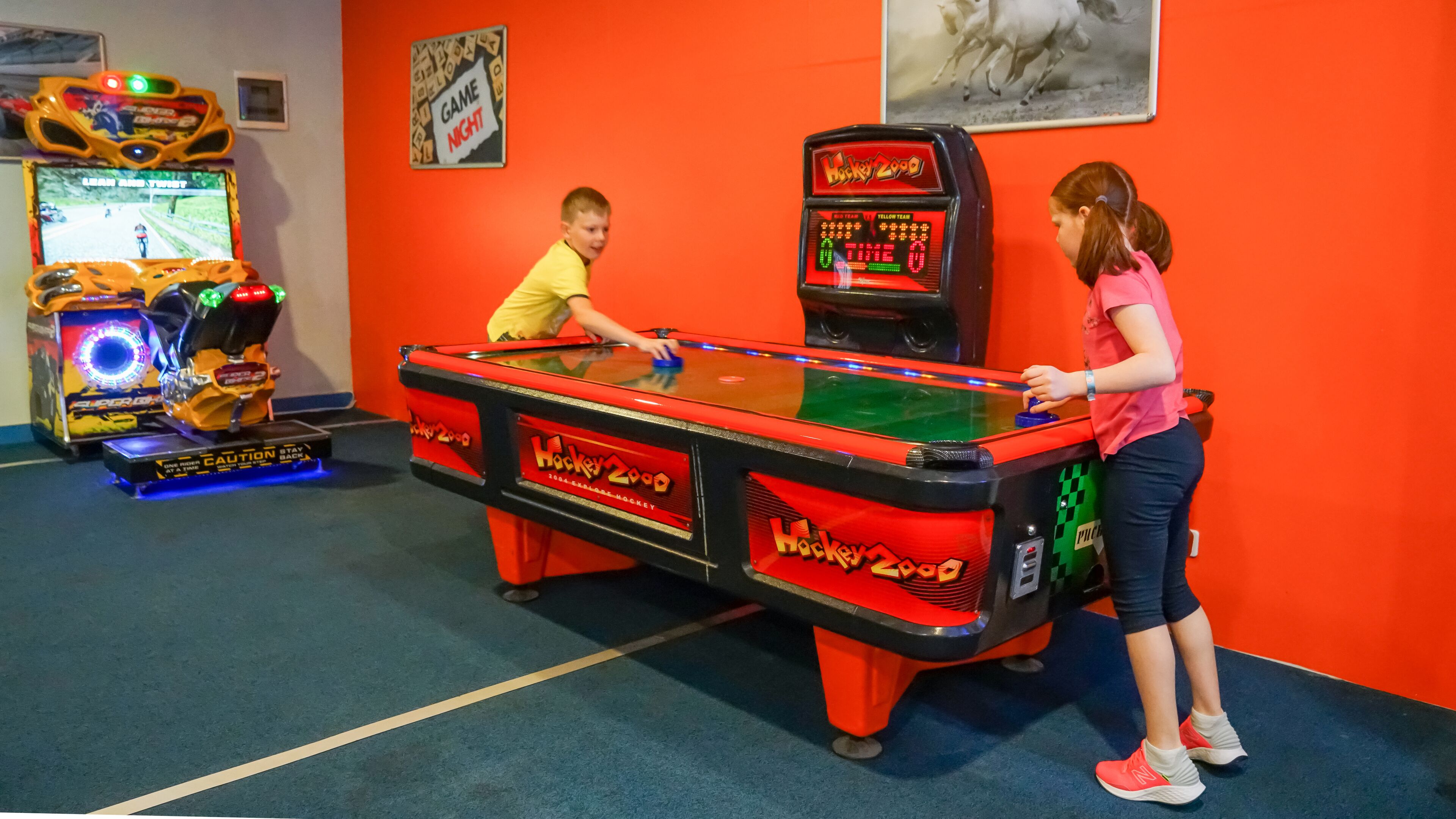 A pool table in a brightly lit room with arcade games in the background.