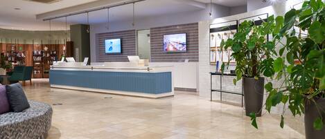 A modern reception area with a blue counter, a seating area with a patterned sofa, and a large potted plant.