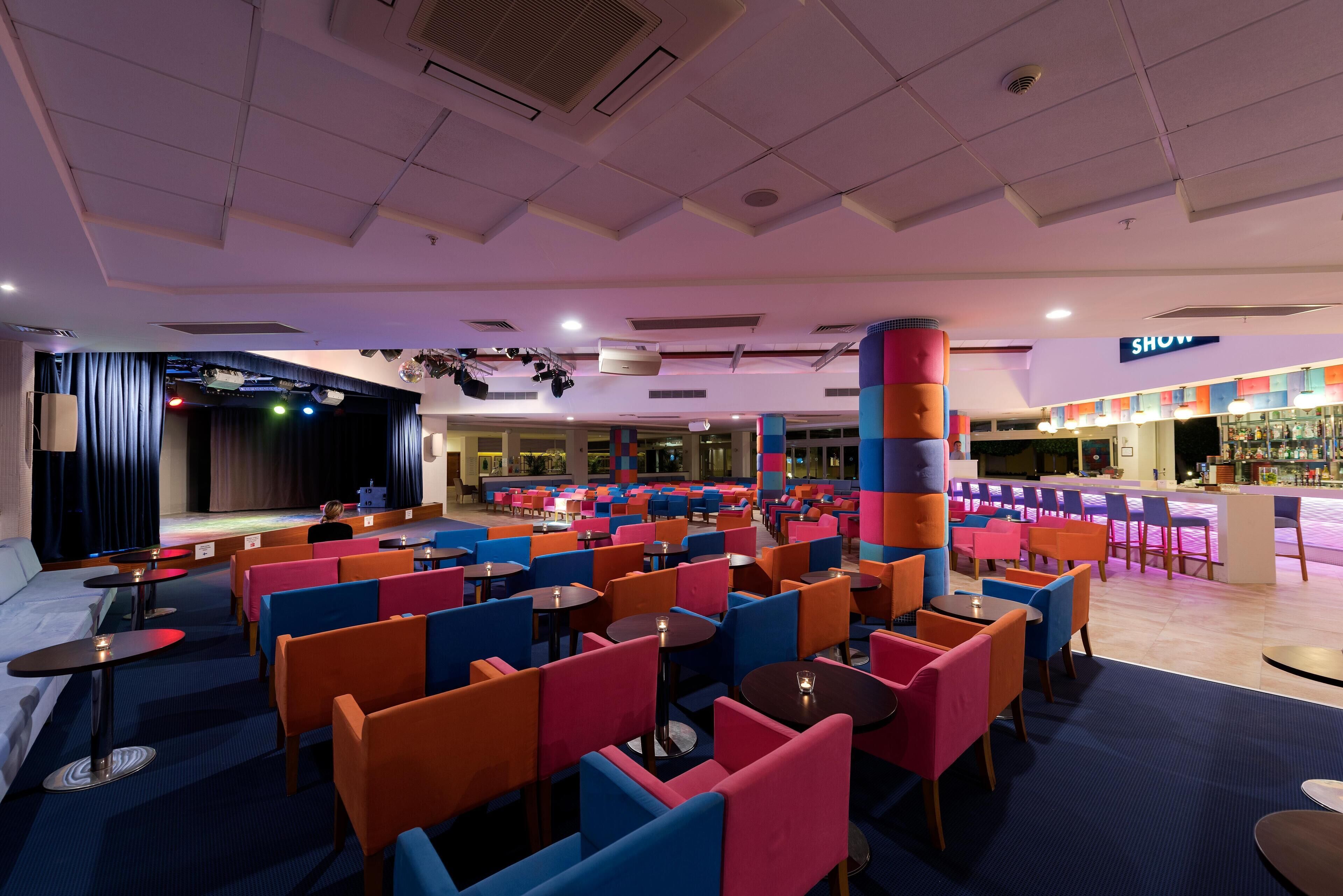 A spacious indoor area with multiple seating arrangements, a stage, and a bar area.
