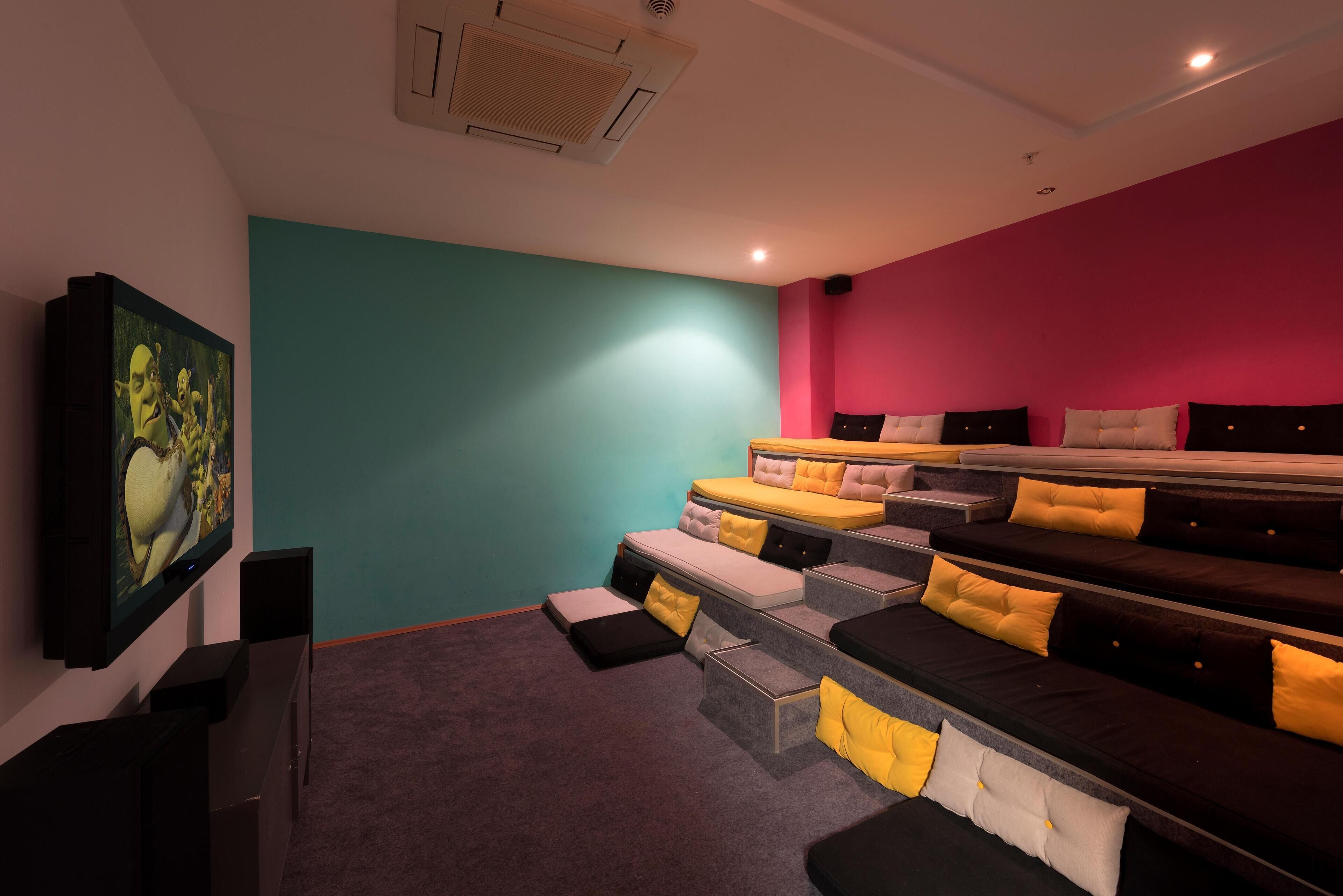 A theater room with tiered seating, a mounted screen, and a red accent wall.