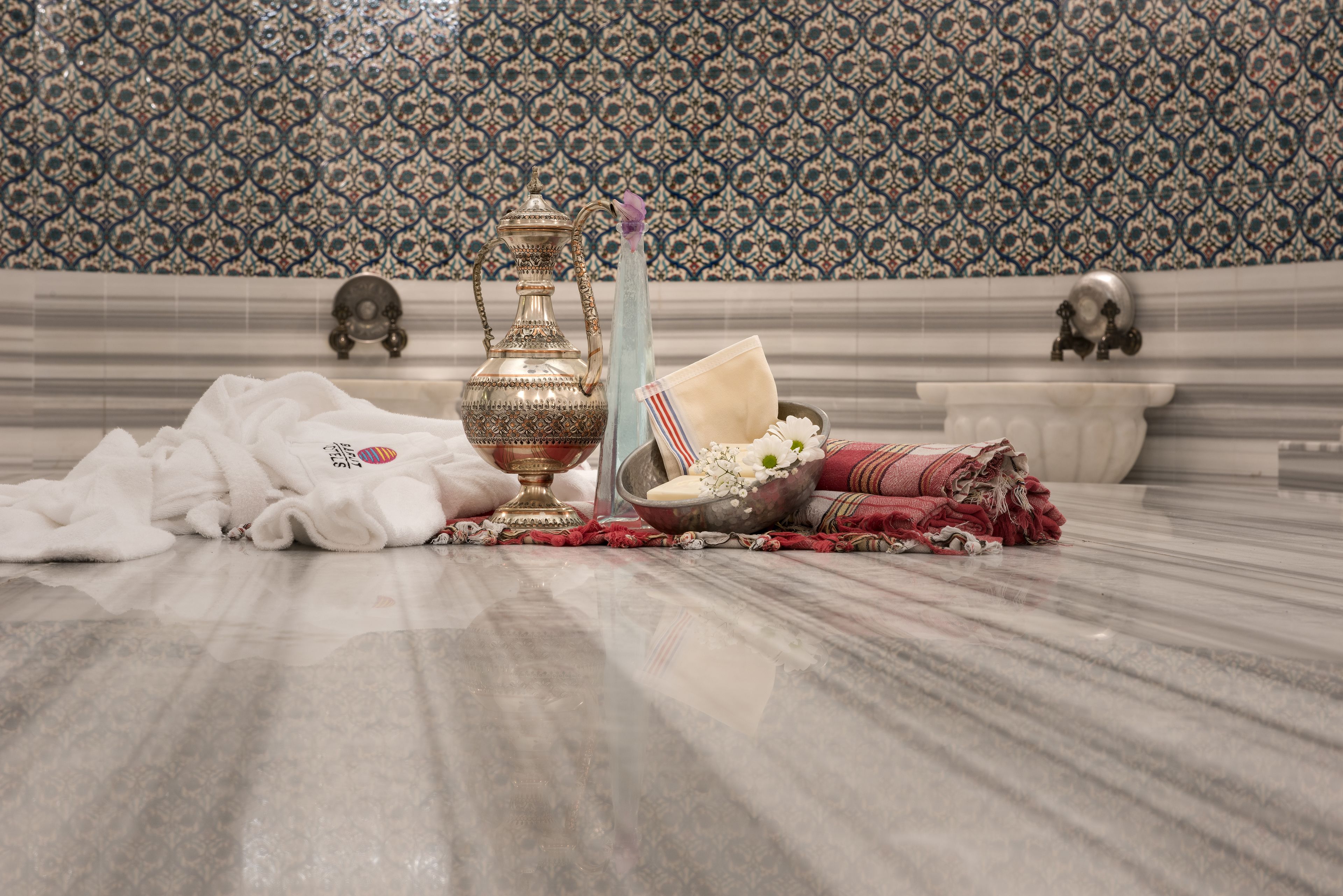A marble floor with a decorative metal pitcher, a bowl with flowers, and a white cloth.