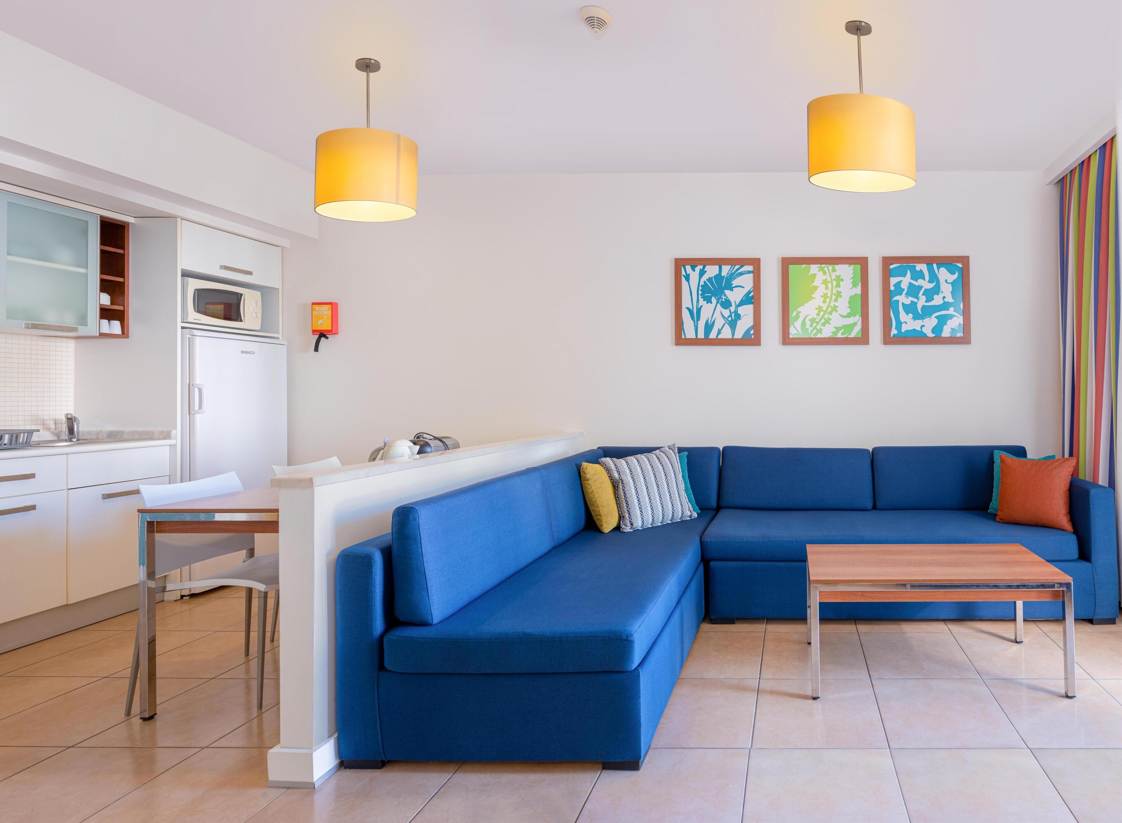 A modern living room with a blue sectional sofa, a wooden coffee table, and two pendant lights.
