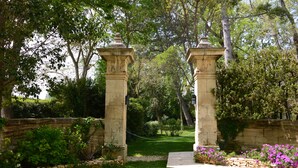 Un jardín con pilares de piedra, un muro de piedra y un sendero que atraviesa abundante vegetación.