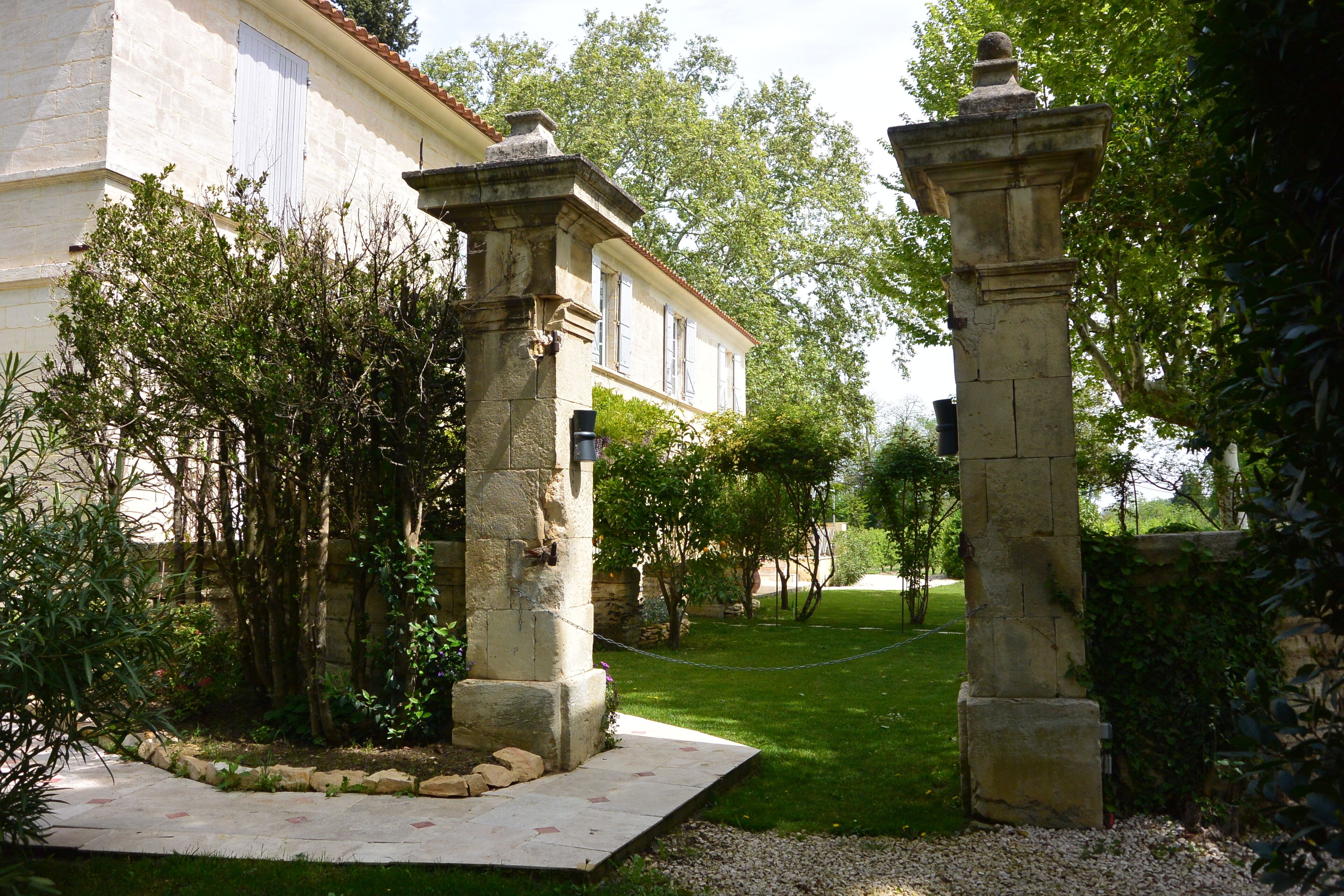 Un patio con pilares de piedra, un edificio blanco y abundante vegetación.