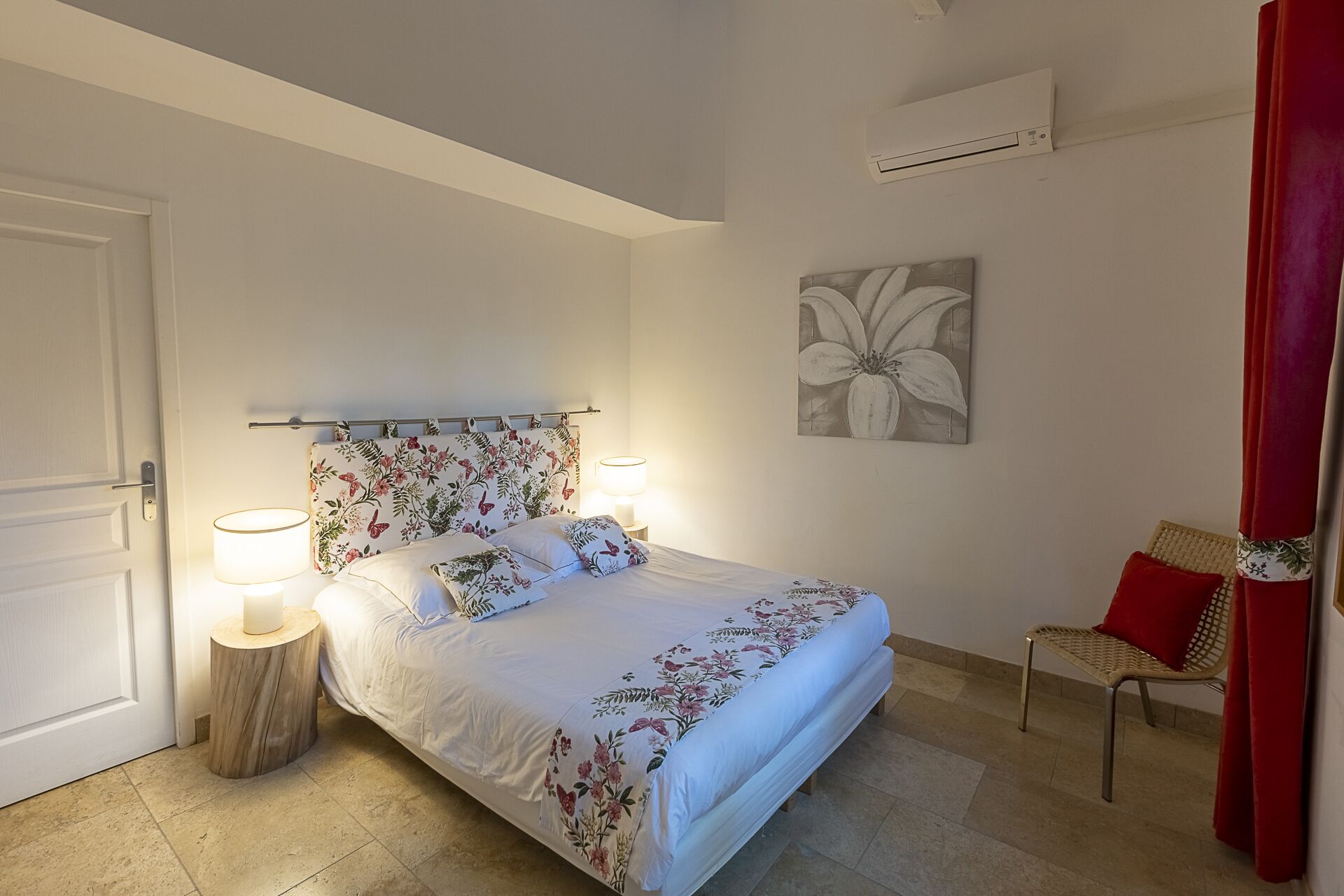 Un dormitorio con cama, lámparas de noche, una silla, una puerta y un aire acondicionado instalado en la pared.