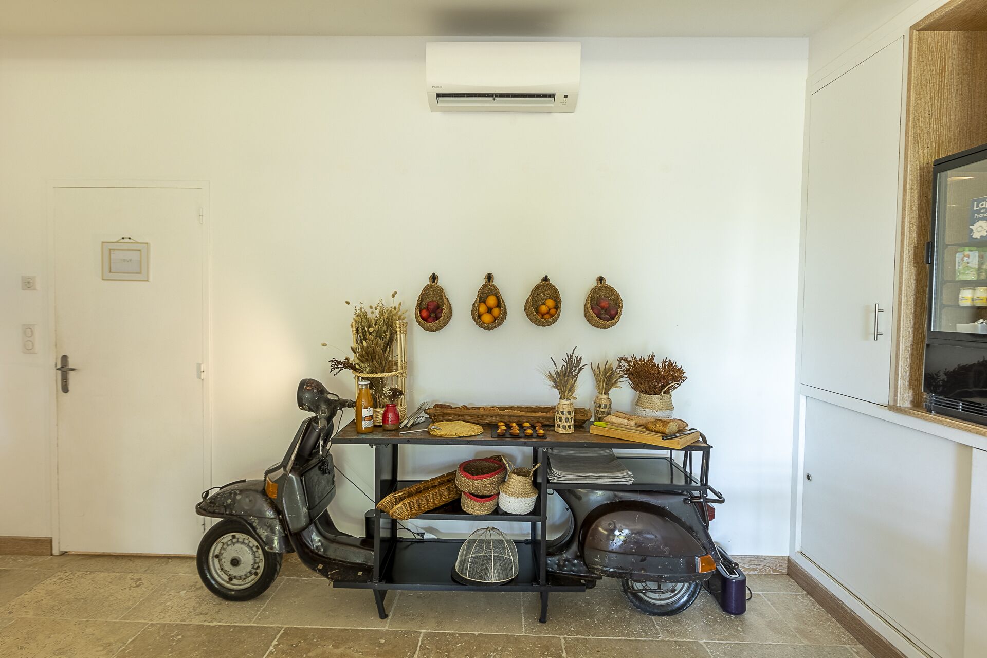 A compact room with a scooter, a small table with various items, a wall-mounted air conditioner, and a door with a sign.