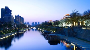 A river with a bridge in the background, surrounded by buildings and a traditional structure with a tiled roof.
