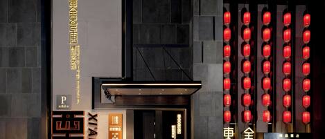 A hotel entrance with a large sign, a modern facade, and a row of red lanterns.